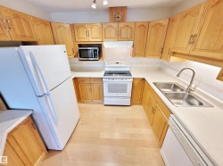 Kitchen with white appliances, light countertops, extractor fan, light brown cabinets, and decorative backsplash - 