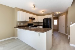 Kitchen with black appliances, dark countertops, white cabinetry, light wood-style flooring, and a textured ceiling - 