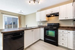 Kitchen featuring a peninsula, black appliances, dark countertops, white cabinets, and under cabinet range hood - 
