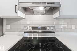 Kitchen view of under cabinet range hood, decorative backsplash, electric range, and light stone countertops - 