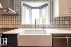 Kitchen featuring wall chimney range hood, light stone countertops, black range, dishwasher, and tasteful backsplash - 