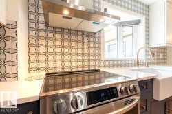 Kitchen view of under cabinet range hood, stainless steel electric stove, tasteful backsplash, light stone countertops, and white cabinets - 