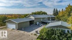 View of front of home featuring dirt driveway, a deck, a garage, a patio, and roof with shingles - 