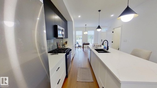 Kitchen with stainless steel appliances, a large island with sink, pendant lighting, light wood-style flooring, and tasteful backsplash - 11308 128 Street, Edmonton, AB - Indoor Photo Showing Kitchen With Double Sink With Upgraded Kitchen