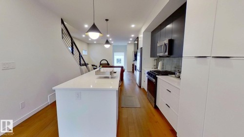 Kitchen with an island with sink, stainless steel appliances, decorative light fixtures, modern cabinets, and light wood finished floors - 11308 128 Street, Edmonton, AB - Indoor Photo Showing Kitchen With Upgraded Kitchen