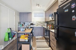 Kitchen featuring black appliances, light countertops, light wood-style flooring, decorative backsplash, and modern cabinets - 