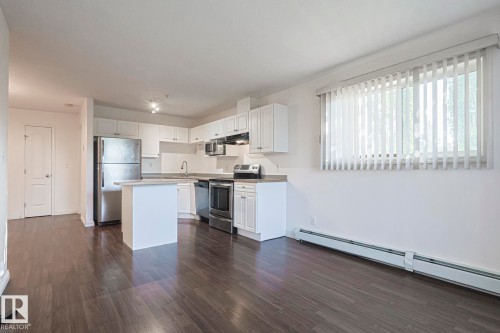 Kitchen with stainless steel appliances, a baseboard heating unit, a kitchen island, and white cabinets - 120 7511 171 Street Nw, Edmonton, AB - Indoor Photo Showing Kitchen