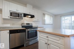 Kitchen featuring stainless steel appliances, white cabinets, under cabinet range hood, and dark wood finished floors - 