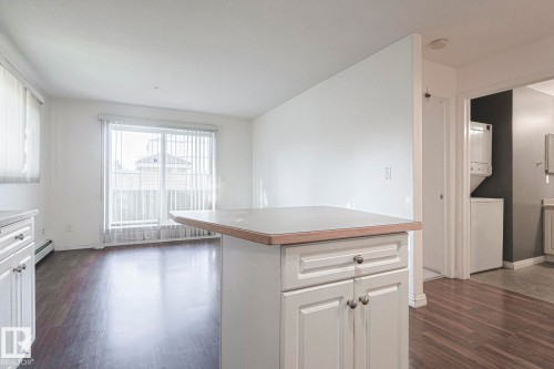 Kitchen featuring dark wood-type flooring, white cabinets, a center island, stacked washer / drying machine, and a baseboard heating unit - 120 7511 171 Street Nw, Edmonton, AB - Indoor