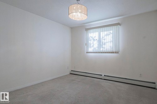 Carpeted empty room featuring baseboard heating and a chandelier - 120 7511 171 Street Nw, Edmonton, AB - Indoor Photo Showing Other Room
