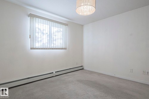 Spare room with a baseboard radiator, carpet, and a chandelier - 120 7511 171 Street Nw, Edmonton, AB - Indoor Photo Showing Other Room