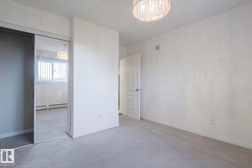 Unfurnished bedroom with light carpet, a closet, a baseboard heating unit, and a chandelier - 120 7511 171 Street Nw, Edmonton, AB - Indoor Photo Showing Other Room