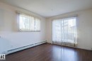 Unfurnished room featuring a baseboard radiator, healthy amount of natural light, and dark wood-style floors - 120 7511 171 Street Nw, Edmonton, AB  - Indoor Photo Showing Other Room 