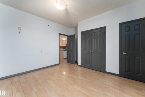 Unfurnished bedroom with multiple closets, light wood finished floors, and a textured ceiling - 101 6220 134 Avenue, Edmonton, AB - Indoor Photo Showing Other Room