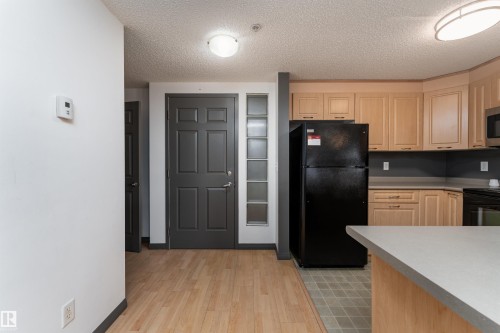 Kitchen featuring light brown cabinets, black appliances, light countertops, a textured ceiling, and light wood-style flooring - 101 6220 134 Avenue, Edmonton, AB - Indoor Photo Showing Kitchen