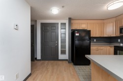 Kitchen featuring light brown cabinets, black appliances, light countertops, a textured ceiling, and light wood-style flooring - 