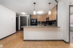 Kitchen featuring black appliances, light brown cabinetry, light countertops, light wood finished floors, and a textured ceiling - 