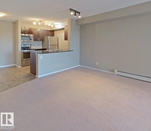 Kitchen featuring dark countertops, appliances with stainless steel finishes, open floor plan, a peninsula, and light carpet - 404 5370 Chappelle Road, Edmonton, AB - Indoor Photo Showing Kitchen