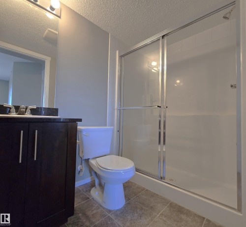 Bathroom with vanity, a textured ceiling, light tile patterned floors, and a shower stall - 404 5370 Chappelle Road, Edmonton, AB - Indoor Photo Showing Bathroom