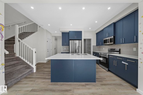 Kitchen with blue cabinets, appliances with stainless steel finishes, an island with sink, recessed lighting, and light wood-type flooring - 1813 Collip View View, Edmonton, AB - Indoor Photo Showing Kitchen With Stainless Steel Kitchen With Upgraded Kitchen