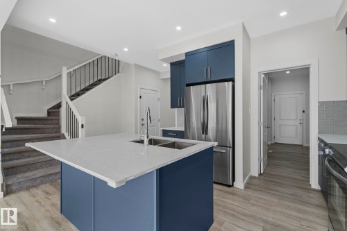 Kitchen featuring blue cabinetry, an island with sink, freestanding refrigerator, light stone counters, and recessed lighting - 1813 Collip View View, Edmonton, AB - Indoor Photo Showing Kitchen With Stainless Steel Kitchen With Double Sink With Upgraded Kitchen