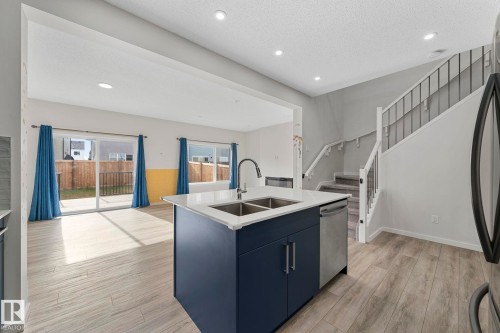 Kitchen with recessed lighting, light wood finished floors, a kitchen island with sink, blue cabinetry, and stainless steel dishwasher - 1813 Collip View View, Edmonton, AB - Indoor Photo Showing Kitchen With Double Sink
