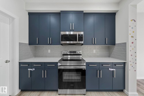 Kitchen featuring appliances with stainless steel finishes, modern cabinets, light stone countertops, light wood finished floors, and backsplash - 1813 Collip View View, Edmonton, AB - Indoor Photo Showing Kitchen