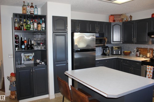 Kitchen with a center island, stainless steel appliances, light countertops, a textured ceiling, and open shelves - 5221 54A Street, Elk Point, AB - Indoor Photo Showing Kitchen