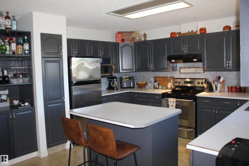 Kitchen featuring appliances with stainless steel finishes, a breakfast bar area, a center island, light countertops, and a textured ceiling - 5221 54A Street, Elk Point, AB - Indoor Photo Showing Kitchen