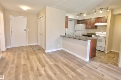 Kitchen featuring white appliances, a textured ceiling, a peninsula, dark countertops, and under cabinet range hood - 