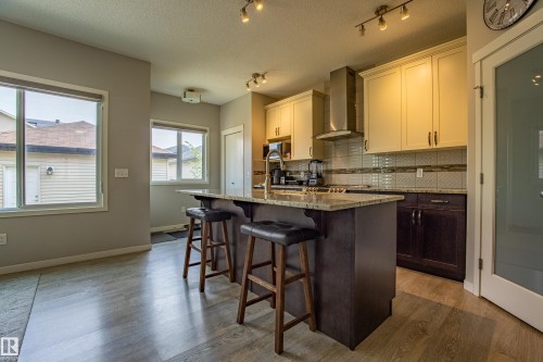Kitchen featuring tasteful backsplash, dark brown cabinetry, a kitchen breakfast bar, a textured ceiling, and wall chimney exhaust hood - 2407 Casey Link, Edmonton, AB - Indoor Photo Showing Kitchen