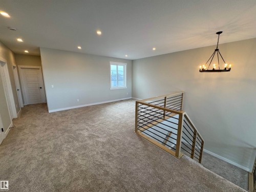 Carpeted empty room featuring a chandelier and baseboards - 28 Harley Way, Spruce Grove, AB - Indoor Photo Showing Other Room