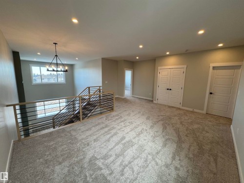 Carpeted empty room featuring baseboards and hanging lights - 28 Harley Way, Spruce Grove, AB - Indoor Photo Showing Other Room