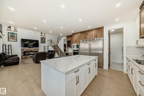 Kitchen featuring a stone fireplace, open floor plan, light wood-style flooring, built in appliances, and a center island - 42 Elwyck Gate, Spruce Grove, AB - Indoor Photo Showing Kitchen With Upgraded Kitchen