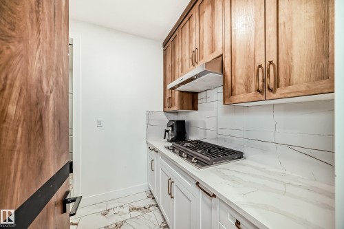 Kitchen with tasteful backsplash, light marble finish floors, stainless steel gas stovetop, light stone counters, and under cabinet range hood - 42 Elwyck Gate, Spruce Grove, AB - Indoor Photo Showing Kitchen