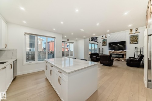 Kitchen featuring white cabinetry, a glass covered fireplace, open floor plan, light wood-style flooring, and a center island - 42 Elwyck Gate, Spruce Grove, AB - Indoor Photo Showing Kitchen