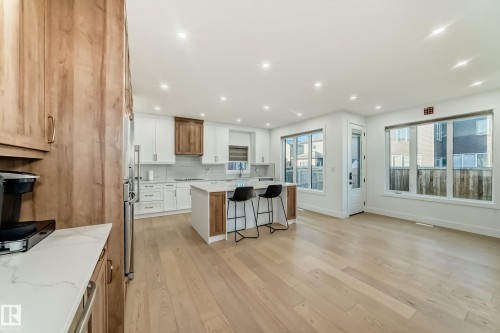 Kitchen with white cabinets, a kitchen breakfast bar, brown cabinetry, light wood-style flooring, and a kitchen island - 42 Elwyck Gate, Spruce Grove, AB - Indoor Photo Showing Kitchen With Upgraded Kitchen