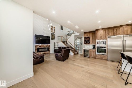 Living room featuring a glass covered fireplace, light wood-style floors, stairs, wine cooler, and recessed lighting - 42 Elwyck Gate, Spruce Grove, AB - Indoor Photo Showing Kitchen With Stainless Steel Kitchen