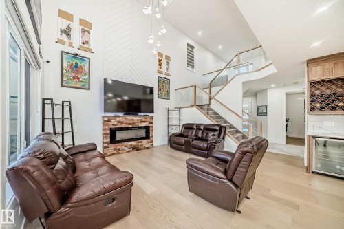 Living area featuring light wood-type flooring, a high ceiling, wine cooler, stairs, and a glass covered fireplace - 42 Elwyck Gate, Spruce Grove, AB - Indoor With Fireplace