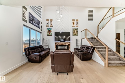 Living area featuring a glass covered fireplace, stairway, light wood-style floors, and a high ceiling - 42 Elwyck Gate, Spruce Grove, AB - Indoor Photo Showing Other Room With Fireplace