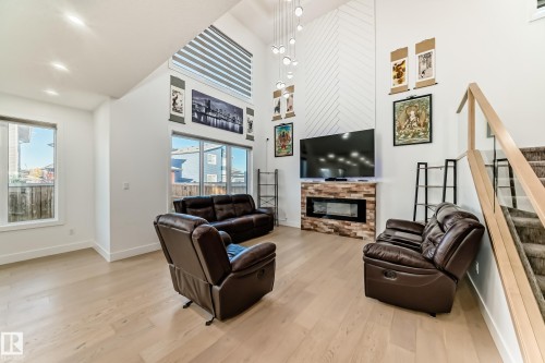 Living room featuring stairs, light wood finished floors, a glass covered fireplace, a high ceiling, and recessed lighting - 42 Elwyck Gate, Spruce Grove, AB - Indoor Photo Showing Other Room With Fireplace