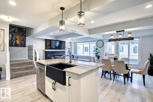 Kitchen featuring beam ceiling, white cabinets, pendant lighting, a stone fireplace, and a center island with sink - 19633 26A Av, Edmonton, AB - Indoor