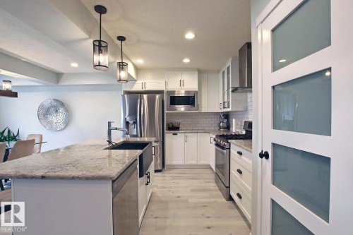 Kitchen with stainless steel appliances, backsplash, wall chimney exhaust hood, white cabinetry, and decorative light fixtures - 19633 26A Av, Edmonton, AB - Indoor Photo Showing Kitchen With Upgraded Kitchen