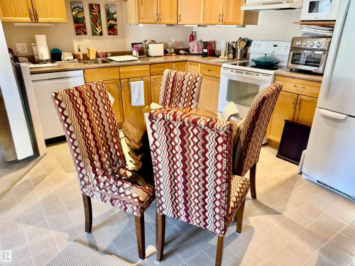 Kitchen with white appliances, light countertops, and under cabinet range hood - 415 4700 43 Avenue, Stony Plain, AB - Indoor Photo Showing Kitchen
