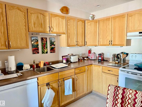 Kitchen featuring white appliances, a textured ceiling, under cabinet range hood, and light brown cabinets - 415 4700 43 Avenue, Stony Plain, AB - Indoor Photo Showing Kitchen With Double Sink