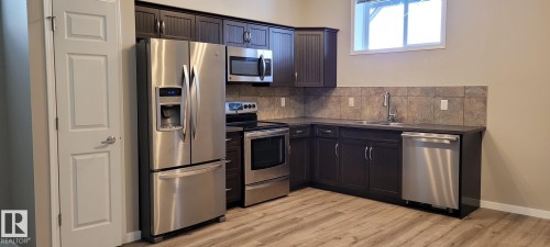 Kitchen with appliances with stainless steel finishes, dark countertops, tasteful backsplash, and light wood-type flooring - 196, 142 Selkirk Place, Leduc, AB - Indoor Photo Showing Kitchen With Double Sink