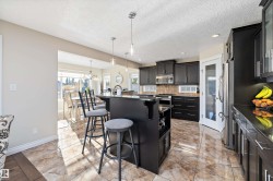 Kitchen featuring a breakfast bar, tasteful backsplash, decorative light fixtures, dark cabinets, and stainless steel appliances - 