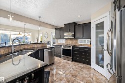 Kitchen with appliances with stainless steel finishes, dark cabinetry, hanging light fixtures, dark stone counters, and recessed lighting - 