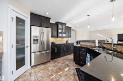 Kitchen featuring arched walkways, stainless steel fridge, hanging light fixtures, glass insert cabinets, and dark cabinetry - 