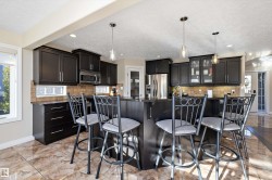 Kitchen with a kitchen breakfast bar, dark cabinets, hanging light fixtures, tasteful backsplash, and a textured ceiling - 